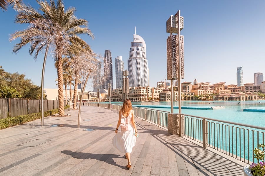 happy tourist girl walking near fountains in dubai city. vacation and sightseeing concept